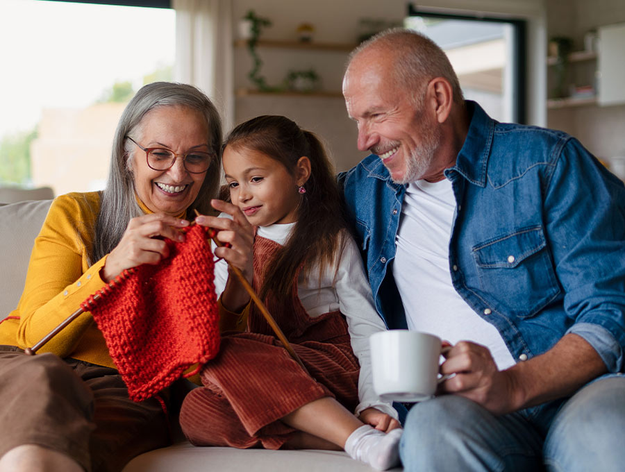 grandparents sitting on the couch with their granddaughter teaching her how to knit retirement future